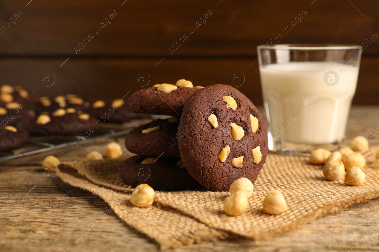 Photo of Tasty chocolate cookies with hazelnuts and milk on wooden table, closeup