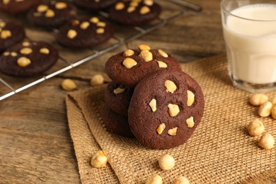 Photo of Tasty chocolate cookies with hazelnuts and milk on wooden table, closeup