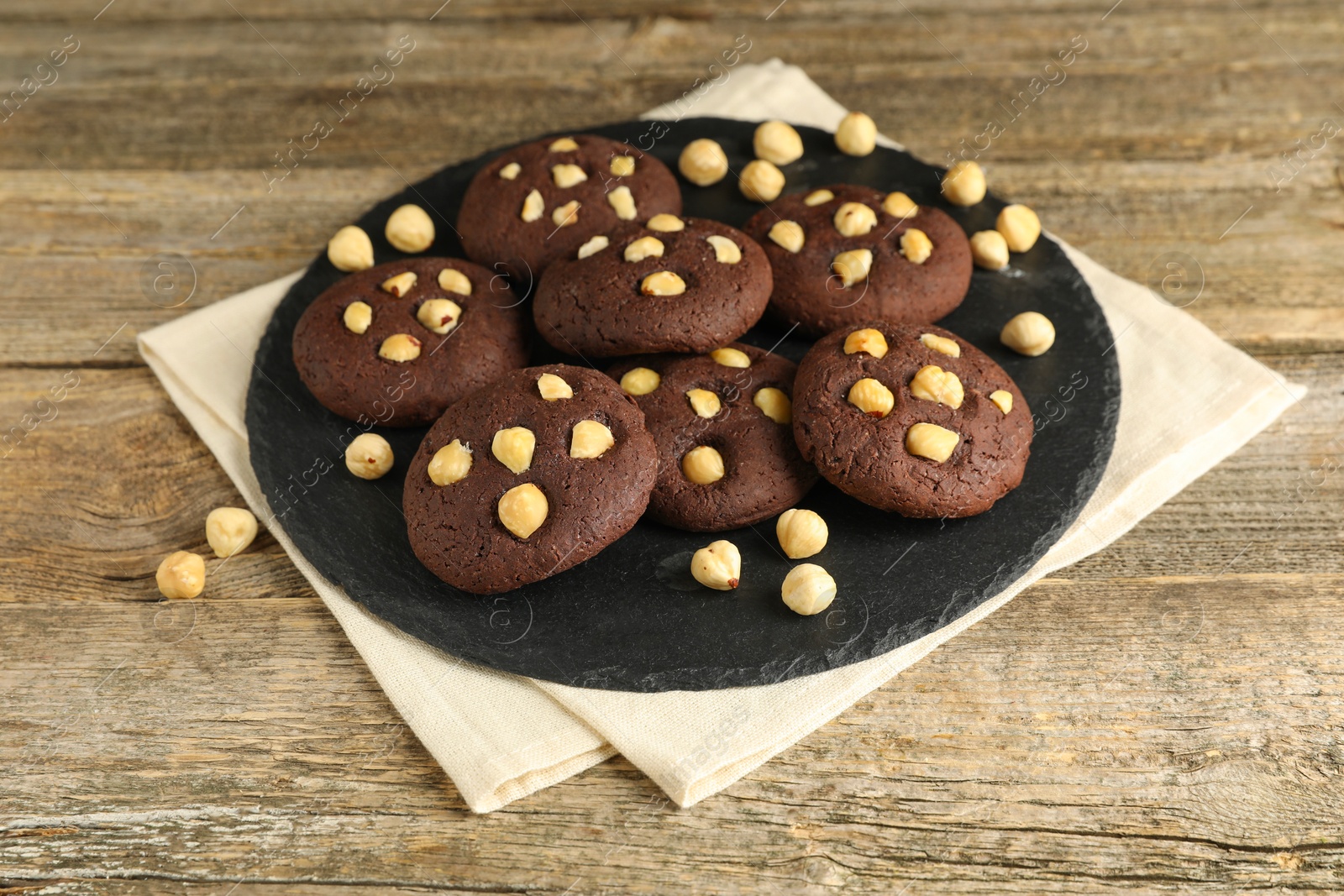 Photo of Tasty chocolate cookies with hazelnuts on wooden table, closeup