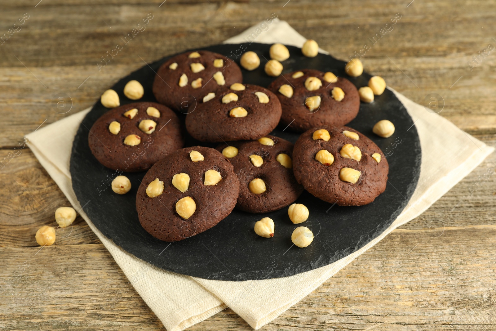 Photo of Tasty chocolate cookies with hazelnuts on wooden table, closeup