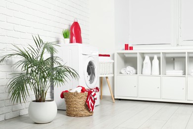 Photo of Washing machine, detergents and basket with laundry in room