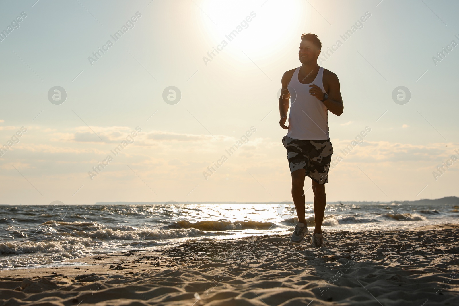 Photo of Sporty man running on sandy beach at sunset