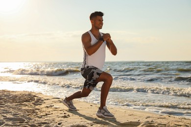 Sporty man doing exercise on sandy beach at sunset