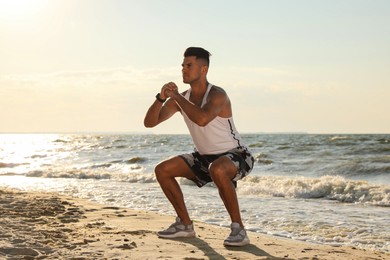 Photo of Sporty man doing exercise on sandy beach at sunset