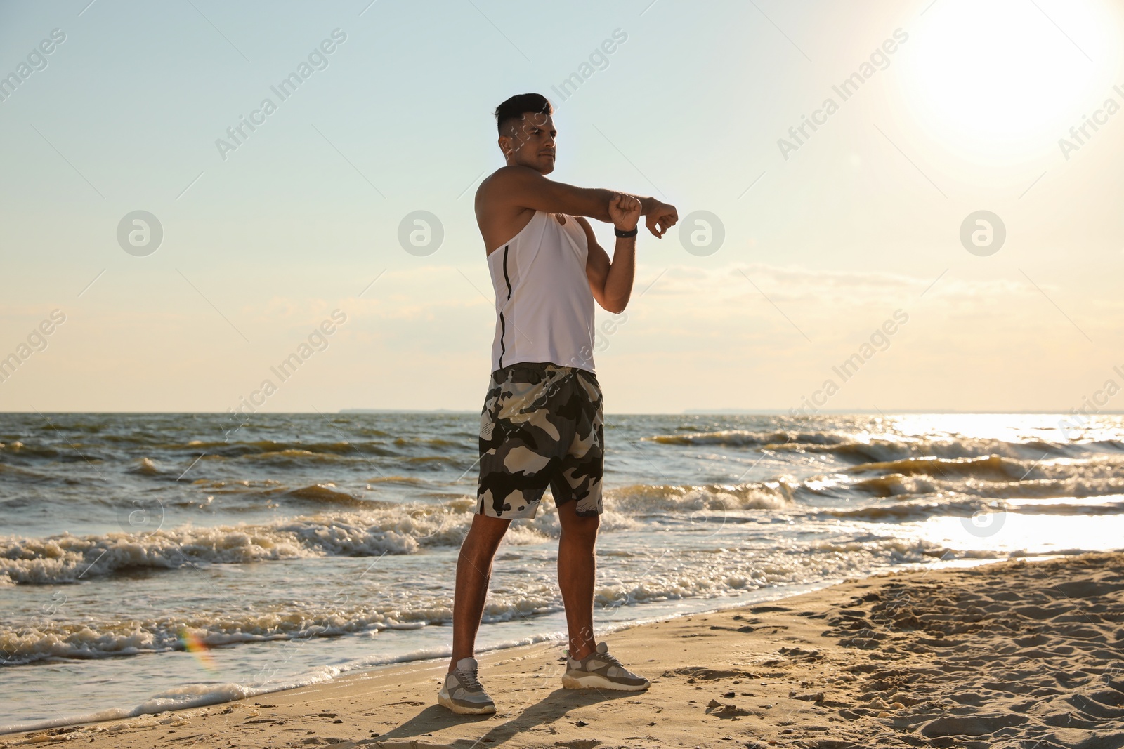 Photo of Sporty man doing exercise on sandy beach at sunset