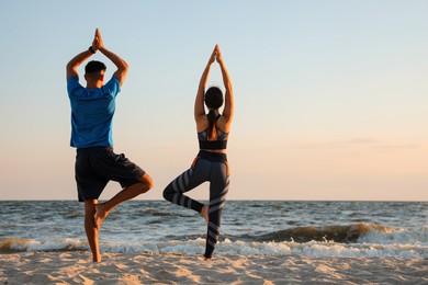 Photo of Couple doing yoga on beach at sunset