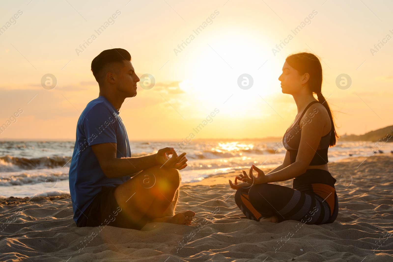 Photo of Couple meditating together on beach at sunset