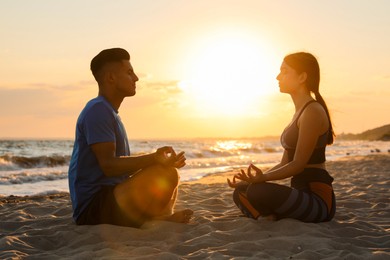 Photo of Couple meditating together on beach at sunset