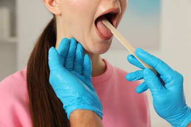 Photo of Doctor examining woman's throat with tongue depressor in clinic, closeup