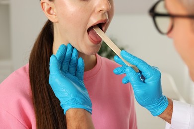 Photo of Doctor examining woman's throat with tongue depressor in clinic, closeup