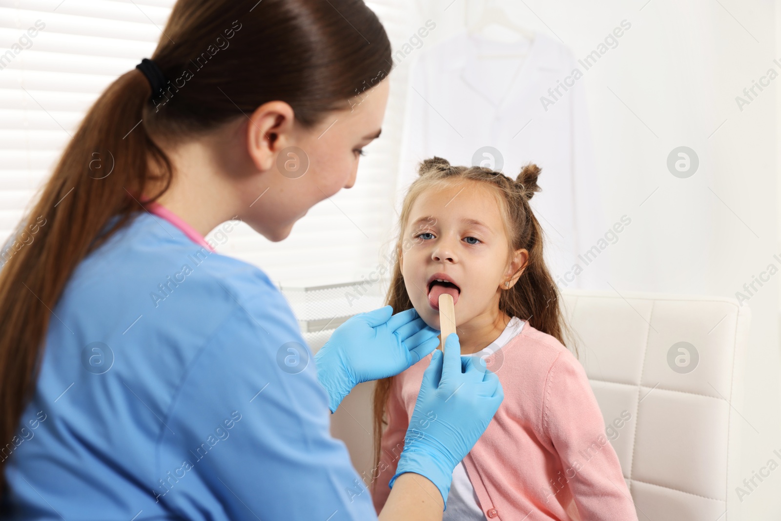 Photo of Doctor examining girl's throat with tongue depressor in clinic