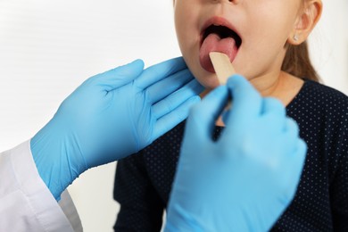 Photo of Doctor examining girl's throat with tongue depressor in clinic, closeup