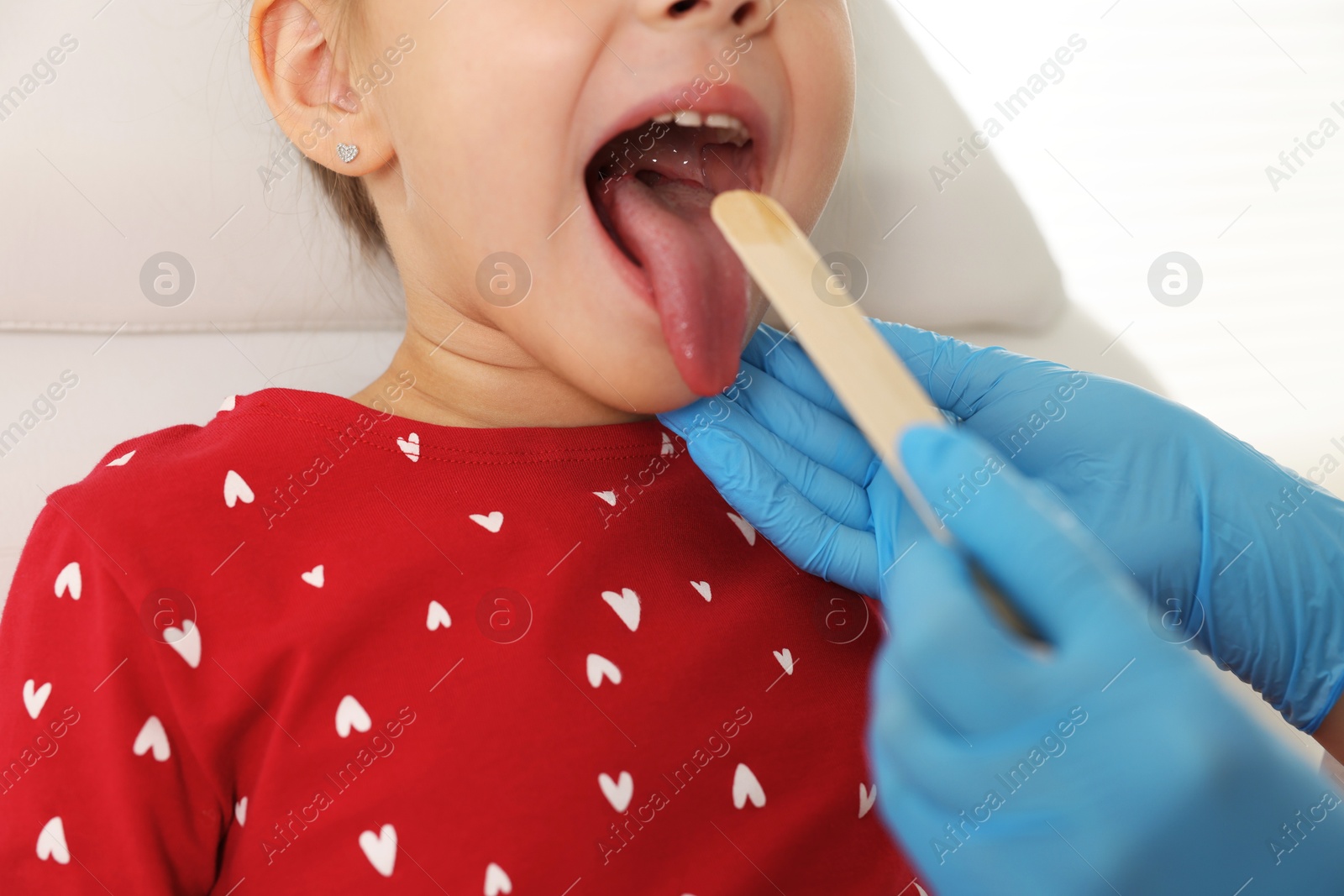 Photo of Doctor examining girl's throat with tongue depressor in clinic, closeup