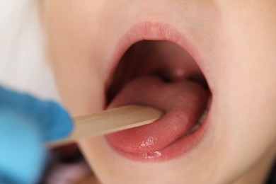 Photo of Doctor examining girl's throat with tongue depressor in clinic, closeup