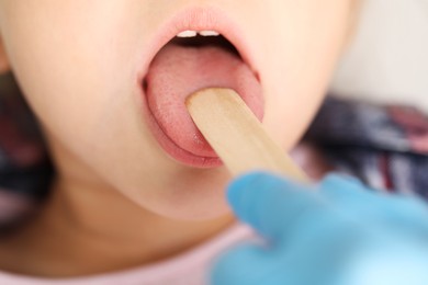 Photo of Doctor examining girl's throat with tongue depressor in clinic, closeup