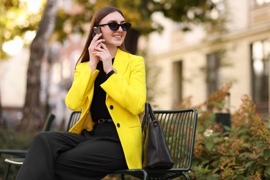 Photo of Smiling businesswoman in stylish suit talking on smartphone outdoors