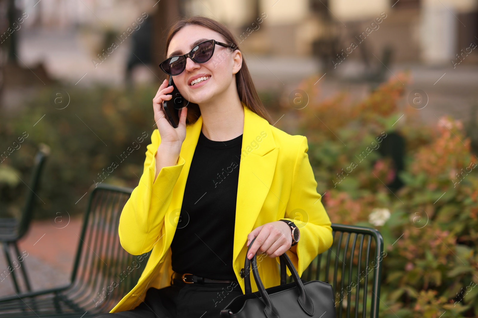 Photo of Smiling businesswoman in stylish suit talking on smartphone outdoors