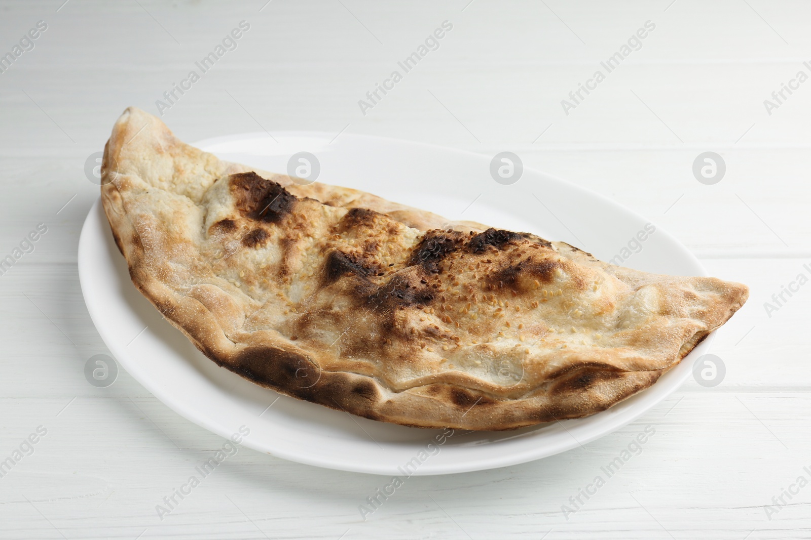 Photo of Plate with tasty calzone on white wooden table, closeup