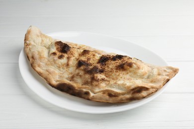 Photo of Plate with tasty calzone on white wooden table, closeup