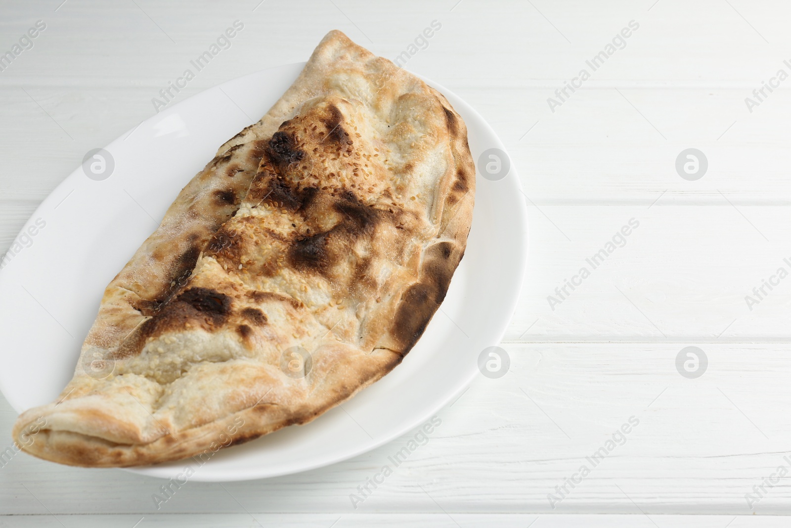 Photo of Plate with tasty calzone on white wooden table, closeup. Space for text