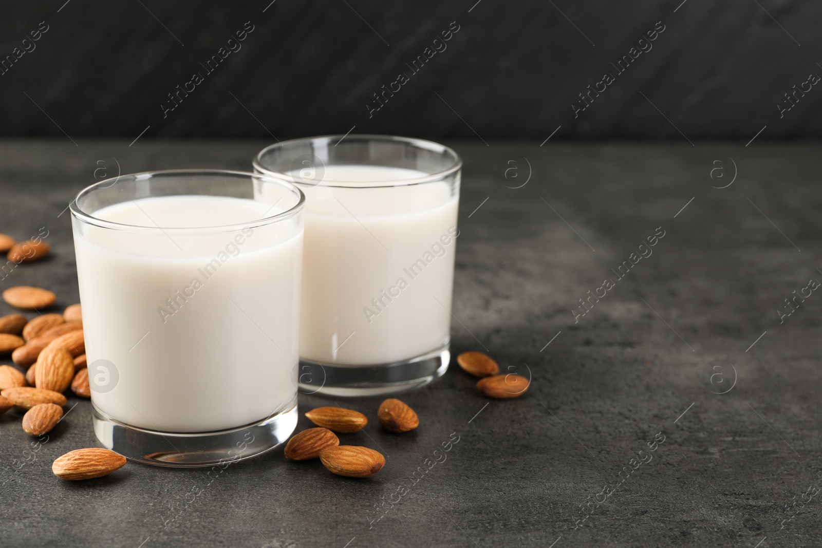 Photo of Fresh almond milk in glasses and nuts on dark grey table, space for text