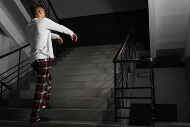 Photo of Young man suffering from sleepwalking on stairs indoors. Space for text