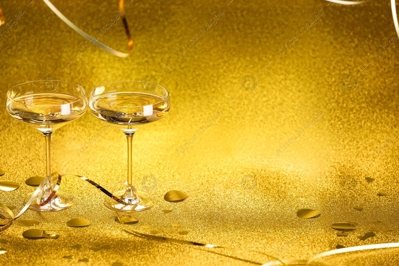 Photo of Champagne in glasses, confetti and streamers on golden background. Space for text