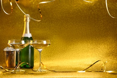 Photo of Champagne in glasses, bottle and ice bucket on golden background. Space for text