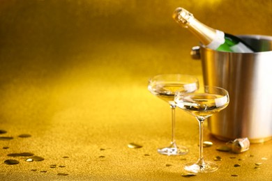 Photo of Champagne in glasses and ice bucket with bottle on golden background. Space for text