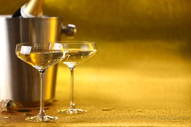 Photo of Champagne in glasses and ice bucket with bottle on golden background. Space for text