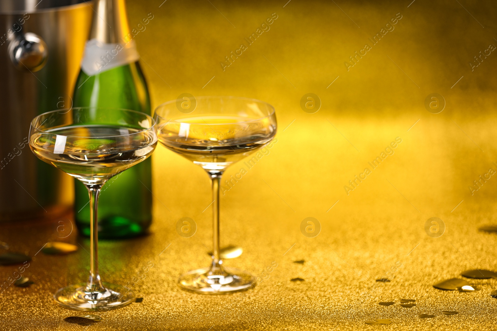 Photo of Champagne in glasses, bottle and ice bucket on golden background. Space for text