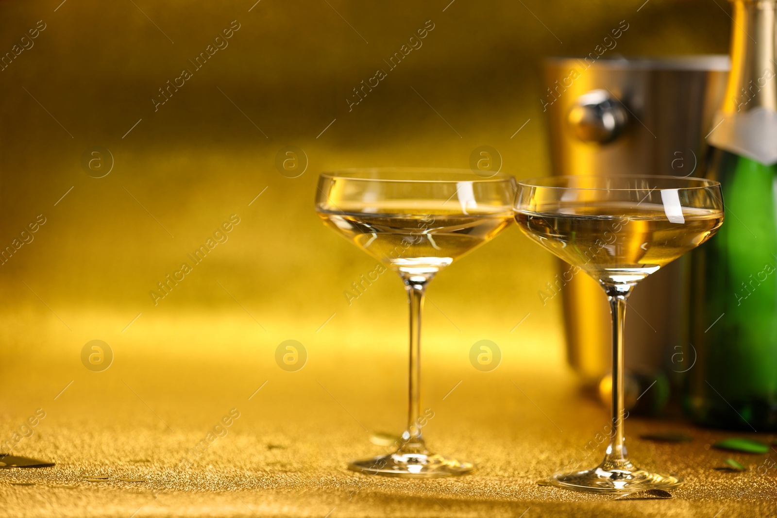 Photo of Champagne in glasses, bottle and ice bucket on golden background. Space for text