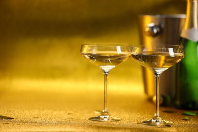 Photo of Champagne in glasses, bottle and ice bucket on golden background. Space for text