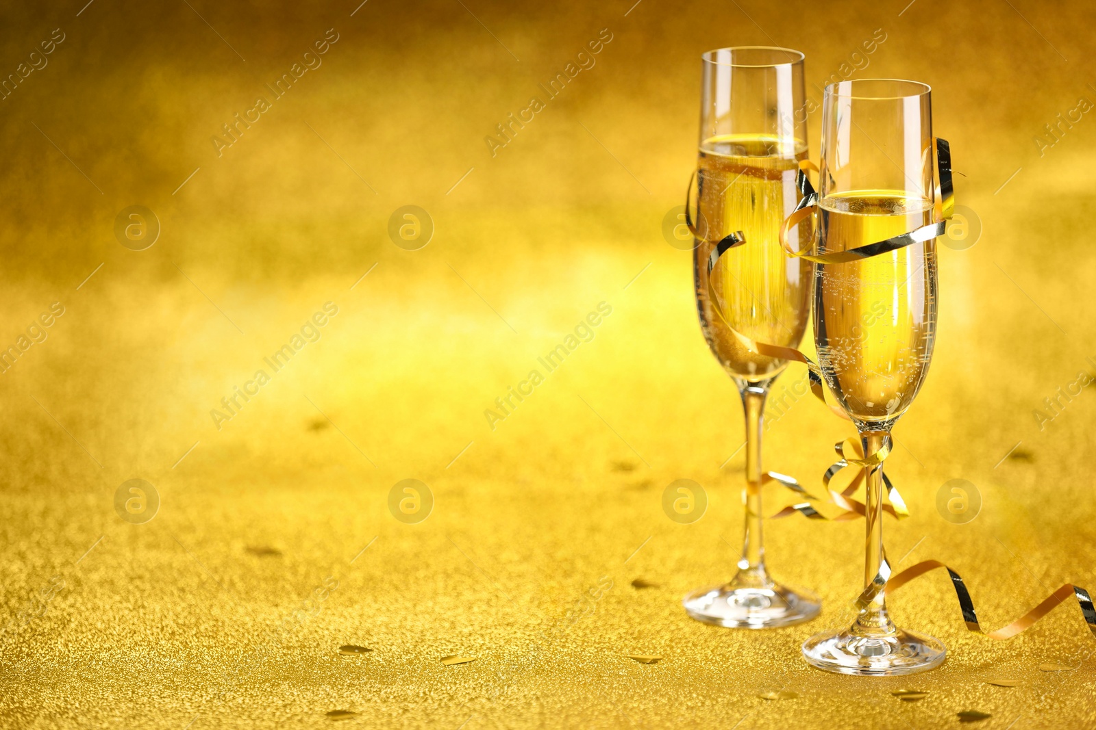 Photo of Champagne in glasses, confetti and streamers on golden background. Space for text