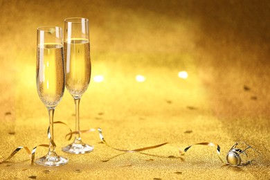 Photo of Champagne in glasses, confetti and streamers on golden background. Space for text