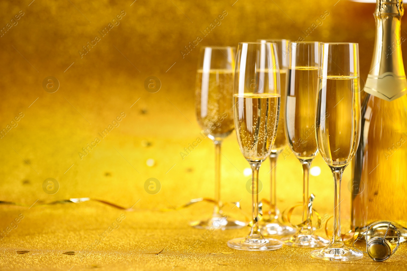 Photo of Champagne, bottle and streamers on golden background. Space for text