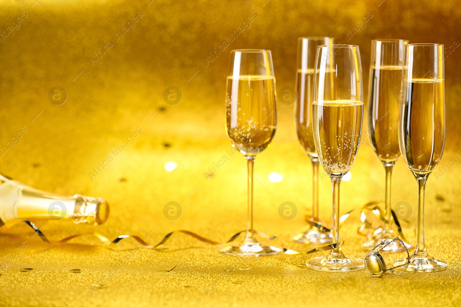 Photo of Champagne, confetti and streamers on golden background. Space for text