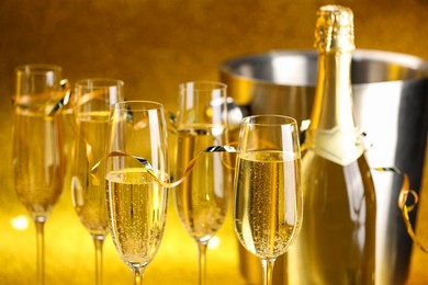 Photo of Champagne in glasses, bottle and ice bucket on golden background, closeup