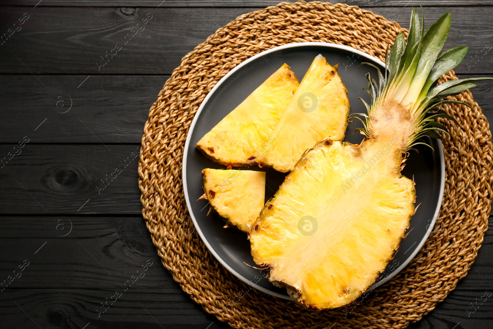 Photo of Cut fresh ripe pineapple on black wooden table, top view. Space for text