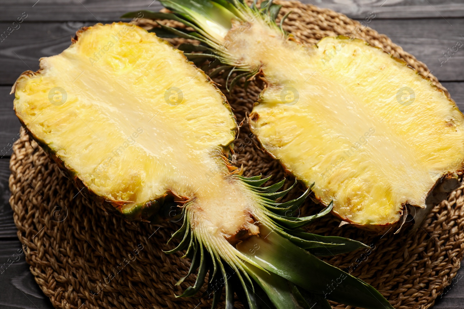 Photo of Halves of ripe pineapple on black wooden table, closeup