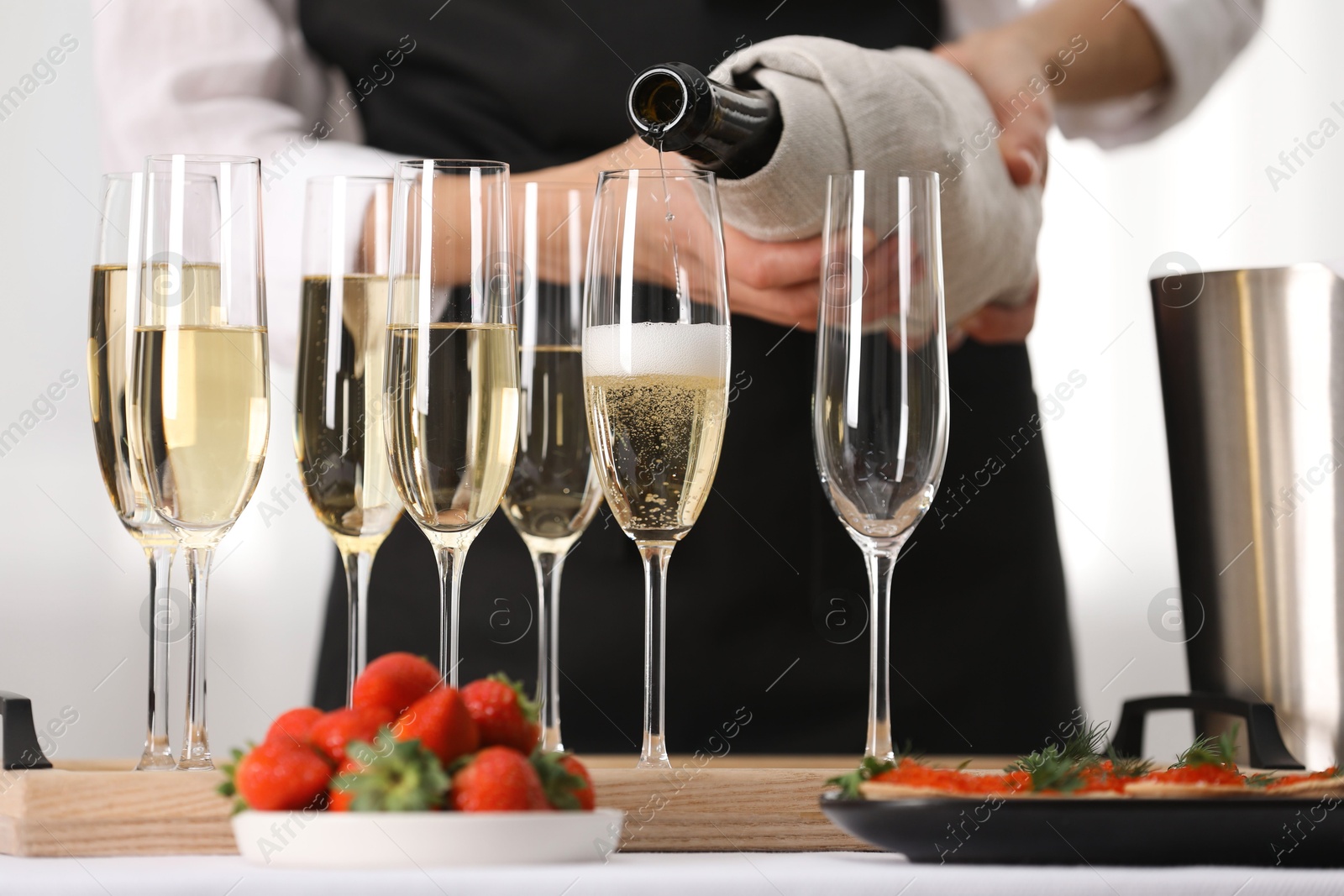 Photo of Waiter filling glasses with champagne indoors, closeup