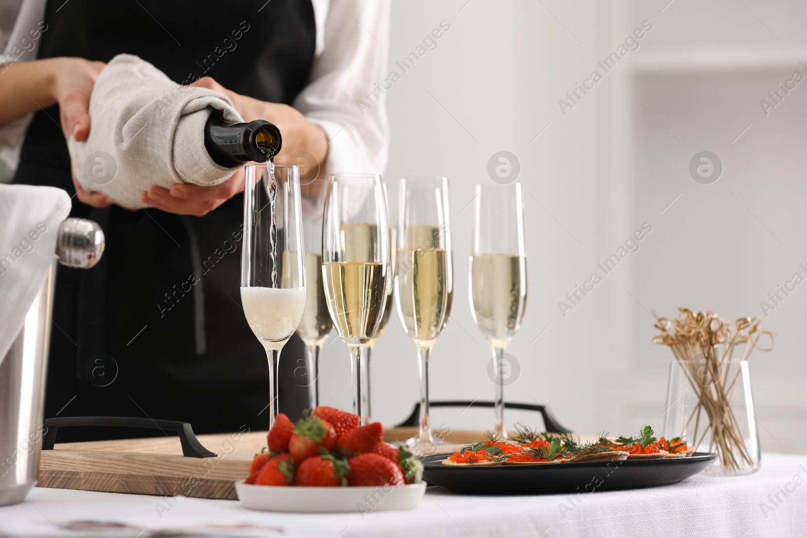 Photo of Waiter filling glasses with champagne indoors, closeup