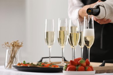 Photo of Waiter filling glasses with champagne indoors, closeup