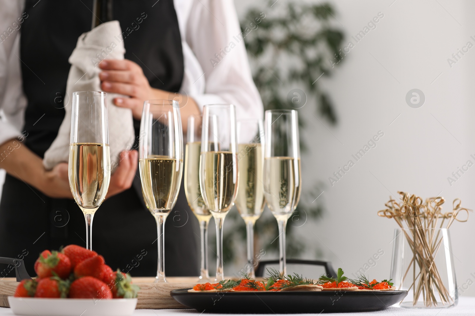 Photo of Waiter with bottle of drink, closeup. Champagne in glasses, strawberries and canapes on table