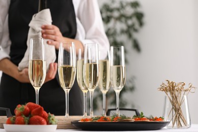 Photo of Waiter with bottle of drink, closeup. Champagne in glasses, strawberries and canapes on table