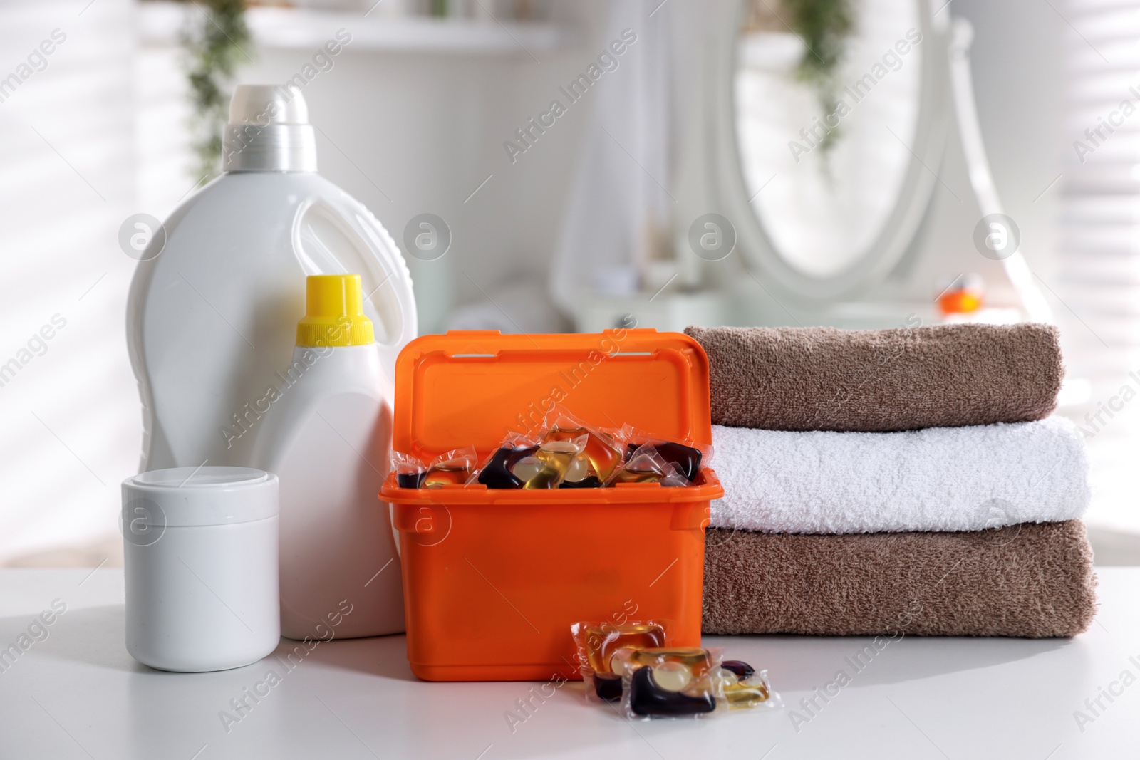 Photo of Laundry capsules, detergents and clean towels on white table in bathroom