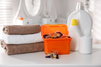 Photo of Laundry capsules, detergents and clean towels on white table in bathroom