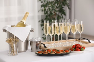 Photo of Champagne, ice bucket, strawberries and canapes with red caviar on white table indoors