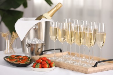 Photo of Champagne, ice bucket, strawberries and canapes with red caviar on white table indoors