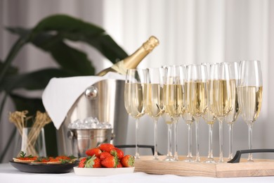 Photo of Champagne, ice bucket, strawberries and canapes with red caviar on white table indoors